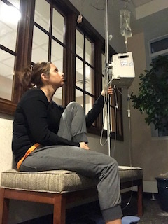 woman holding an iv pole sitting in hospital waiting area forlornly