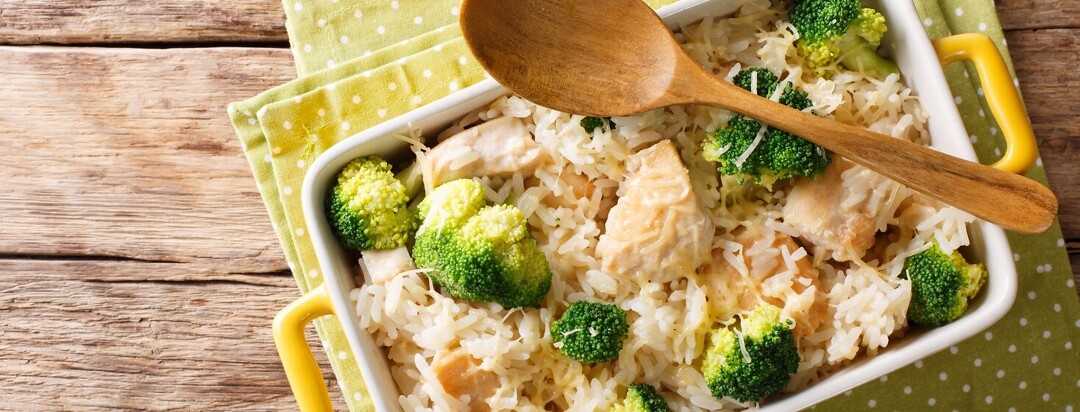 Chicken and rice in a casserole dish with a wooden spoon across the corner.