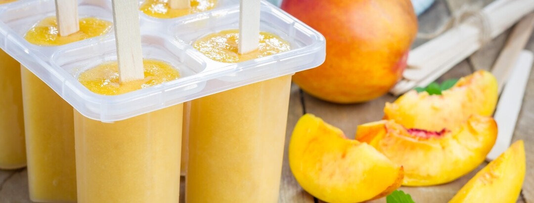 Peach puree in an ice pop mold surrounded by sliced peaches.