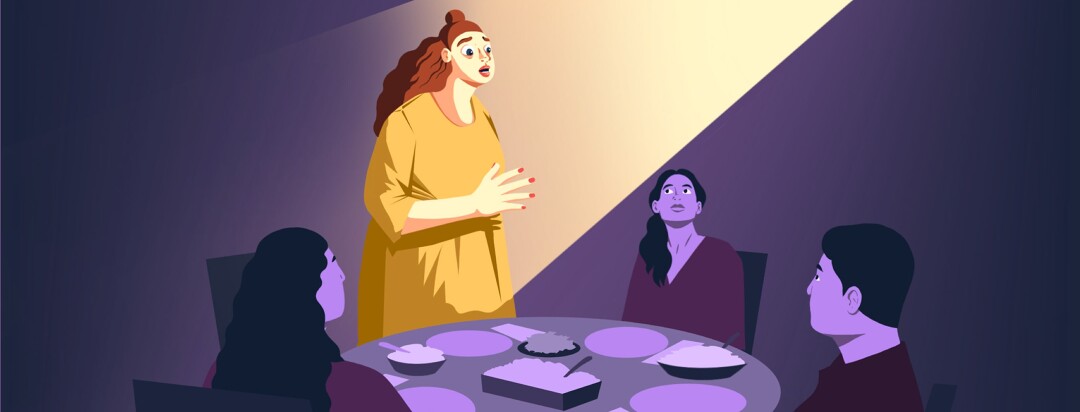 A woman nervously stands and speaks at the dinner table where she is sitting with three other people.