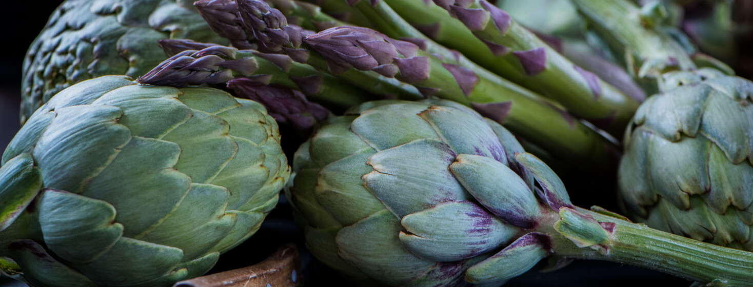 artichokes with knife and asparagus on the rustic textured background