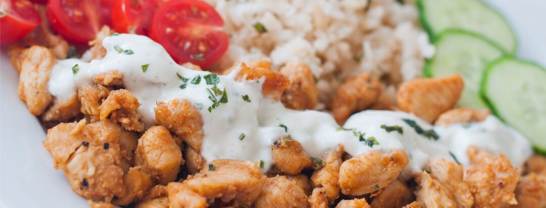 A Greek chicken bowl with rice, cucumber and tomatoes.